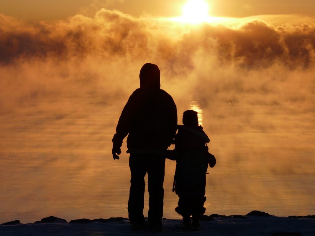 Un homme et un enfant vue de dos regardent le soleil couchant, on devine un look personnel.