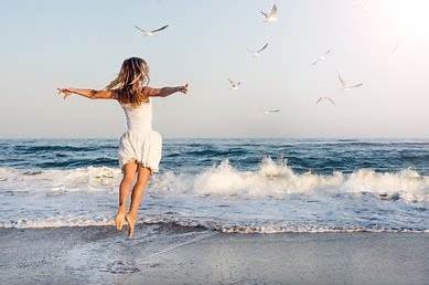 Une fille saute de joie devant la mer, le coaching l'a rend libre.